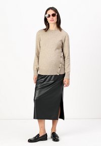 Beige neulepusero, jossa on sivunapit, yhdistetty mustaan tekonahkaiseen midihameeseen, jossa on sivuleikkaus, sekä mustiin loafereihin.