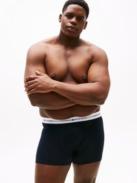 Boxer in navy con elastico bianco con logo "TOMMY HILFIGER"; modello con fisico muscoloso, braccia incrociate.