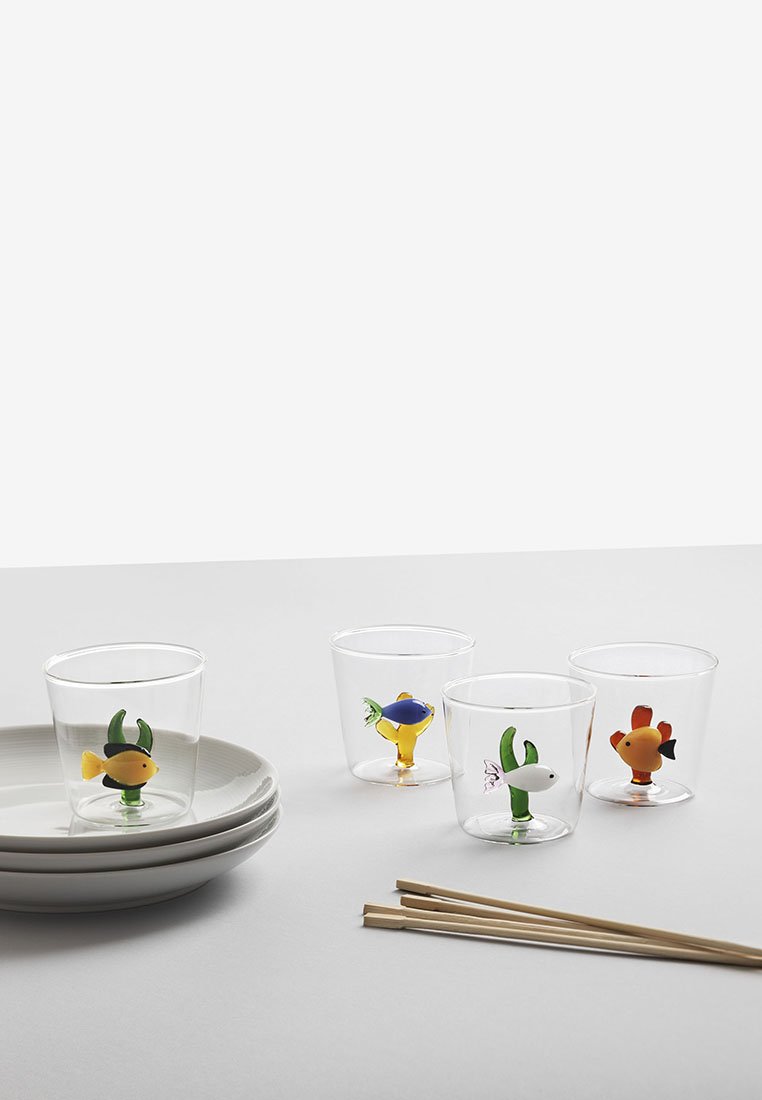 Przezroczyste plastikowe kubki z kolorowymi rybkami na dnie. Zestaw zawiera cztery kubki, stakowane białe talerze oraz bambusowe pałeczki.