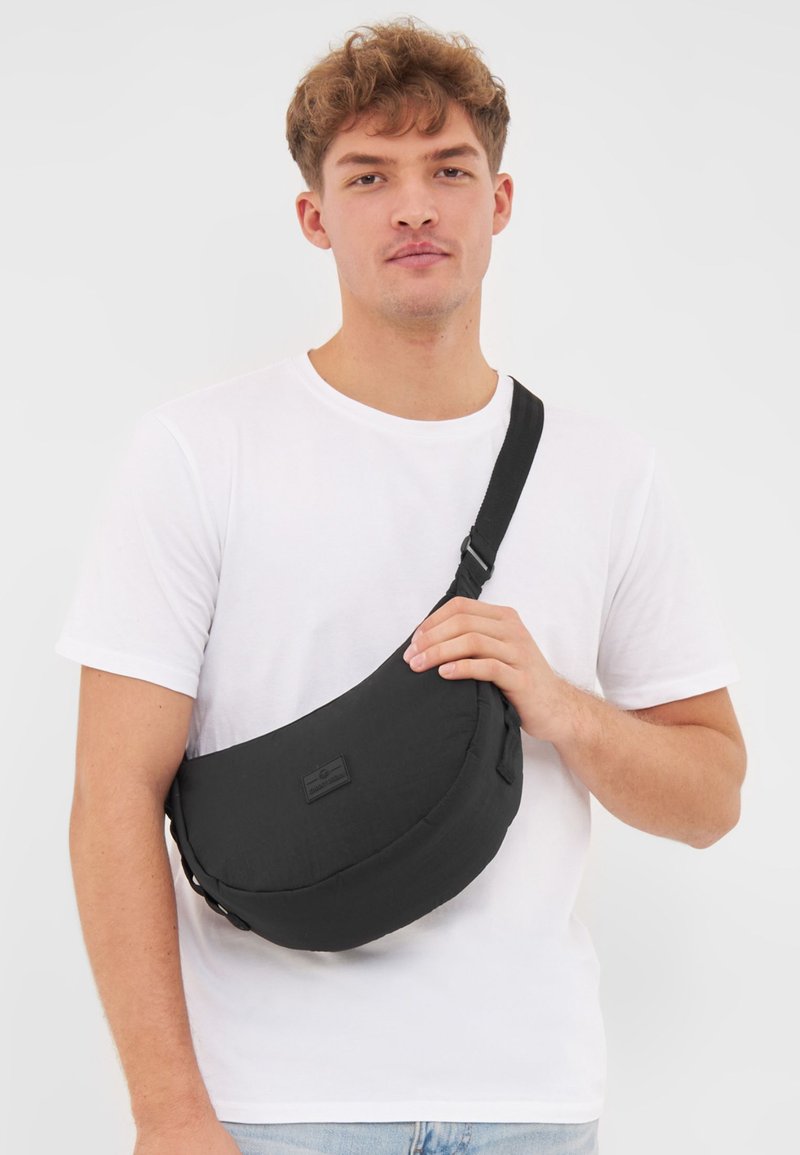 Borsa a spalla nera realizzata in tessuto testurizzato, forma semi-circolare, con tracolla regolabile e un sottile patch con logo.