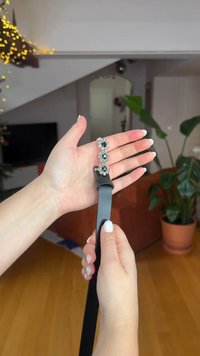 Ceinture en cuir noir avec une boucle décorative en argent ornée d'une pierre noire, tenue dans une main, sur un fond clair et neutre.