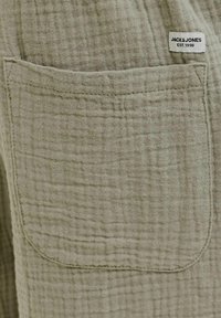 Olivgrüner Stoff mit einer strukturierten Gittermusterung und einer genähten Tasche; enthält ein Etikett mit der Aufschrift "JACK & JONES EST. 1990."