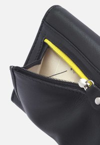 Black leather pouch with a yellow zipper, featuring a beige interior and a simple rectangular shape. Silver hardware is visible on the zip.