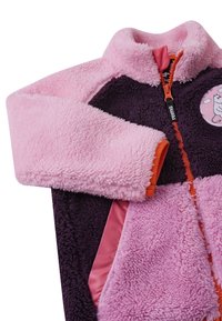 Fleece jacket in pink and purple with a soft texture, high collar, zip front, and a circular patch featuring a character.