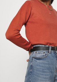 Maglione a maglia color ruggine con scollo rotondo abbinato a jeans di denim azzurri a vita alta e una cintura nera con fibbia rotonda.