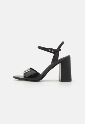 Schwarze Sandale mit dickem Blockabsatz, Knöchelriemen mit Schnalle und vorderem Riemen mit silberner Metallschnallendetail.