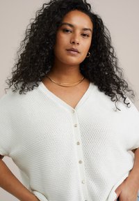 Cardigan en tricot blanc avec un col en V, des manches courtes et des boutons dorés. Présente un motif texturé et une coupe décontractée.