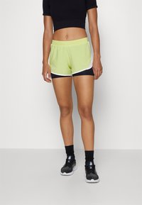 Gröna och svarta kvinnliga idrottsshorts med vit kant, tillverkade av lättviktig tyg, med elastisk midja och en sportig design.