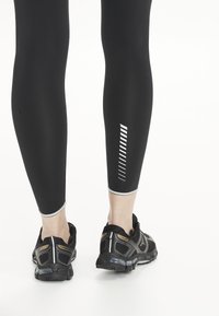 Svarta atletiska leggings med reflekterande ränder och en mjuk textur, tillsammans med svarta löparskor med nätdesign och greppläst.