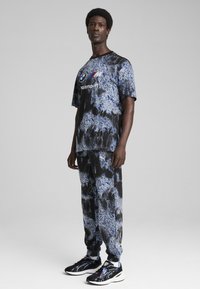 Blå og sort tie-dye træningssæt, der har et logo på trøjen, med tapered bukser og let, struktureret stof. Sorte sportssko.