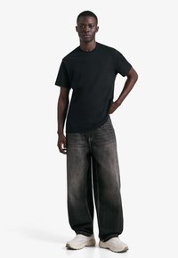 Tricou negru din bumbac cu mâneci scurte, asortat cu blugi largi din denim închis și adidași de culoare deschisă. Design simplu, casual.