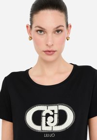 Camiseta negra de cuello redondo con un gran logo blanco hecho de perlas y strass en la parte frontal.