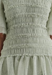 Light green dress featuring a textured, ruched design with layered ruffles at the hem. Made of sheer, lightweight fabric with a delicate pattern.