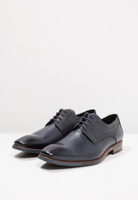 Dark blue leather dress shoes with a polished finish, rounded toe, and standard laces. Features a contrasting brown sole and subtle stitching.