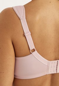 Nahaufnahme des Rückens einer Person, die einen hellrosa BH mit verstellbaren Trägern und einem Hakenverschluss trägt.