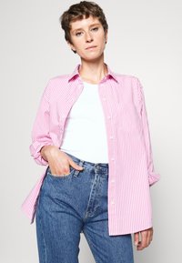 Roze en wit gestreept overhemde met kraag, opgerolde mouwen en een borstzak, gecombineerd met hooggesneden blauwe jeans.