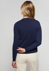 Tmavě modrý svetr s dlouhými rukávy, žebrovanými manžetami a kulatým výstřihem. Hladká textura a přiléhavý střih. Pohled zezadu odhaluje detaily na ramenou.