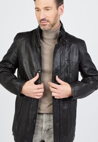 Schwarze Lederjacke mit Stehkragen, Reißverschluss und Druckknopfdetails. Verfügt über Seitentaschen und ein elegantes Design.