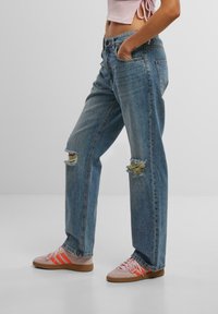 Light blue ripped jeans with a relaxed fit, featuring distressed knees and a classic five-pocket design. Paired with pink sneakers.