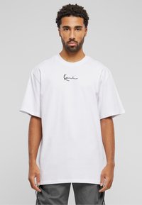 T-shirt en coton blanc à manches courtes, avec un logo noir en signature sur la poitrine. Coupe décontractée et design simple.