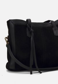 Sac en cuir suédé et en cuir noir avec une texture lisse, doté d'une bandoulière et d'accents en nœud sur le côté, mettant en valeur un design minimaliste.