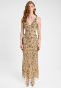 Perlebesat aftenkjole i beige, med en dyb V-halsudskæring, indviklede blomsterdesigns og en tætsiddende silhuet, samt en gennemsigtig overlay og sko med guldaccenter.