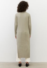 Cardigan lungo a costine in una tonalità verde tenue, realizzato in un tessuto morbido. Presenta maniche lunghe e spacchi laterali per facilitare i movimenti.