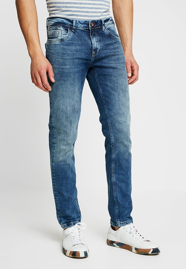 Indigo blauwe jeans met een slim fit, met subtiele vervaging, vijf zakken en een knoopsluiting, gecombineerd met witte sneakers.