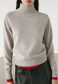 Hellgrauer Rollkragenpullover mit geripptem Kragen und Bündchen. Weiche Textur, eng anliegendes Design, kombiniert mit einer roten Basisschicht und einem schwarzen Lederrock.