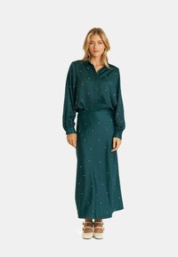 Lange, turkoois satijnen jurk met een ontwerp van een blouse met kraag, versierd met parelachtige embellishments. Gladde textuur en een volledige lengte silhouette.