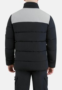 Zwarte pufferjack met grijze bovenkant, voorzien van een gequilt design, hoge kraag en logo patch op de linker mouw.