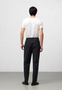 Herenoutfit met een effen wit T-shirt en donkere geplooide broek met een elastische tailleband. Donkere schoenen maken de look compleet.