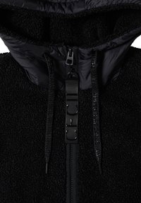 Gros plan d'une veste noire texturée avec une fermeture éclair, des cordons et une capuche doublée d'un tissu lisse.