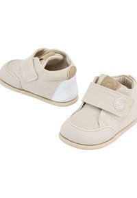 Zapatos para niños pequeños de tela beige con una correa de Velcro, que cuentan con una puntera texturizada, un acento blanco en el talón y una suela de goma ligera.