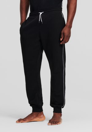 Pantaloni della tuta neri con vita elastica, cordino bianco, tasche laterali, gambe affusolate e piping in contrasto bianco lungo i lati.