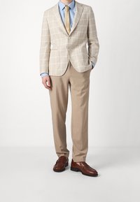 Jasno beżowa marynarka w kratkę, jasnoniebieska koszula, beżowe spodnie, brązowe skórzane loafersy. Strukturalny krój, zapięcie na jeden guzik i klapy w kształcie notcha.