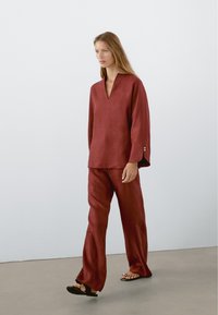 Bordowy zestaw z lnu składający się z luźnej bluzki z dekoltem w serek i spodni o szerokich nogawkach. Posiada rękawy do łokcia oraz guziki jako akcenty.