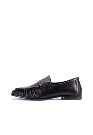 Mocasín de cuero negro con un tacón bajo, diseño delantero plisado y un pequeño logo dorado en el lateral, mostrado desde el lado exterior.