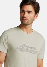 Light green short-sleeve t-shirt made of soft fabric featuring a black mountain and water line graphic across the chest.