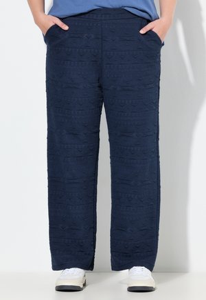 Marineblauwe broek met een gestructureerde geweven stof, voorzien van zijzakken en een rechte snit. Gecombineerd met witte sneakers voor contrast.