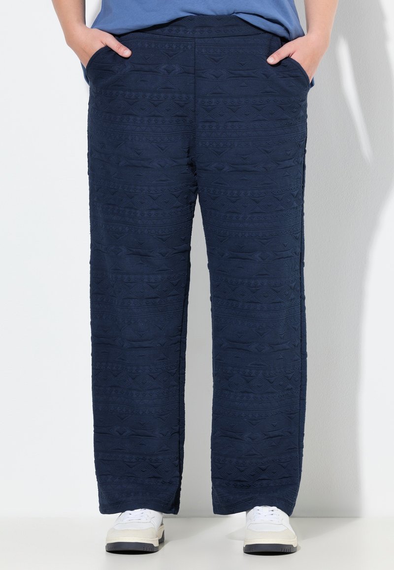 Pantaloni a motivi navy con una trama testurizzata, dotati di tasche laterali e un taglio dritto. Abbinati a sneakers bianche per un contrasto.
