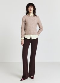 Hellrosa gestrickter Pullover mit rundem Ausschnitt, kombiniert mit einem gelben Hemd mit Kragen, braunen Schlaghosen und bordeauxroten spitzen Schuhen.
