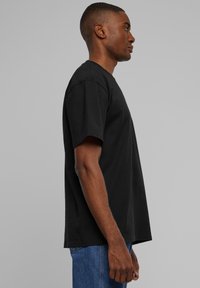 Black, short-sleeve T-shirt made of cotton. Relaxed fit with a crew neckline, visible stitching, and side slits. Worn with blue denim jeans.