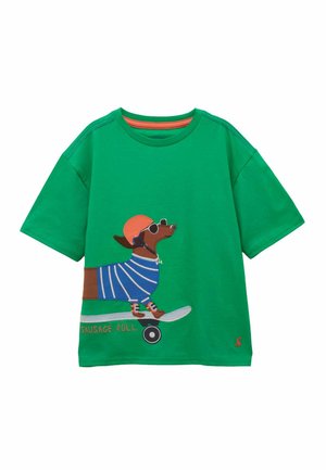 T-shirt vert avec une illustration d'un teckel portant des lunettes de soleil, un casque, un pull rayé et roulant sur un skateboard étiqueté "Sausage Roll".