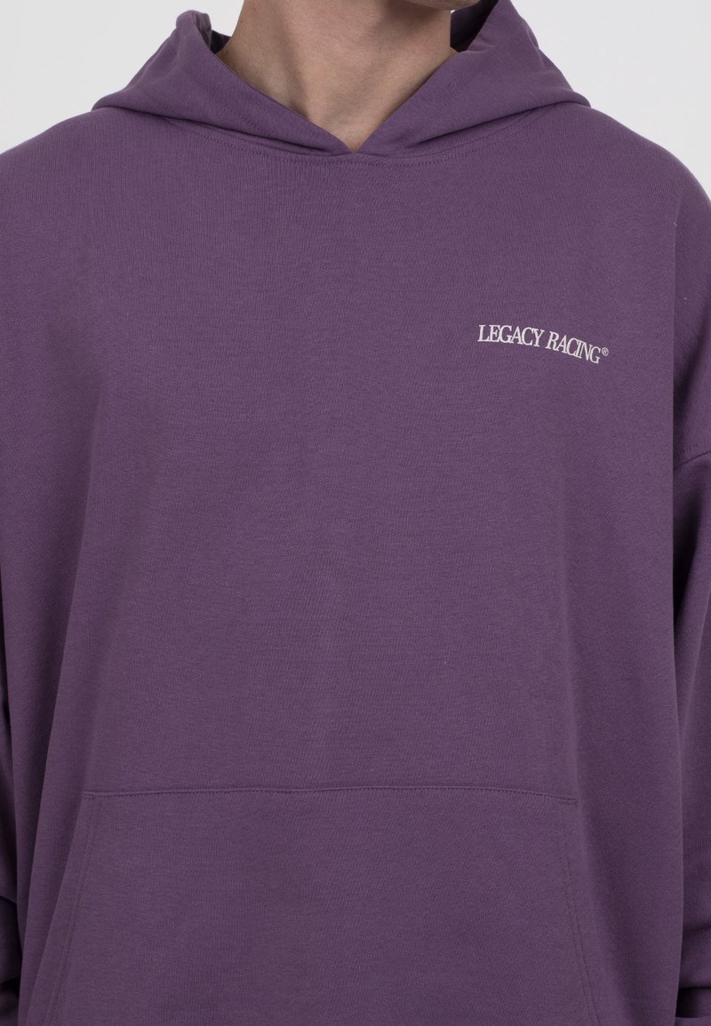 Sweat à capuche violet en tissu doux, avec une poche avant et un logo brodé "LEGACY RACING" blanc sur le côté gauche de la poitrine.