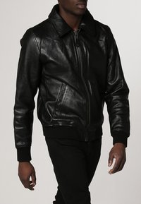 Schwarze Lederbomberjacke mit einem Frontreißverschluss, einem Kragen und zwei seitlichen Taschen. Rippbündchen und -saum mit einer glatten, glänzenden Textur.