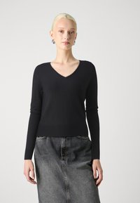Svart, strikket genser med lange ermer og V-hals design. Materialet virker mykt og glatt. Kombinert med et grått denimskjørt.