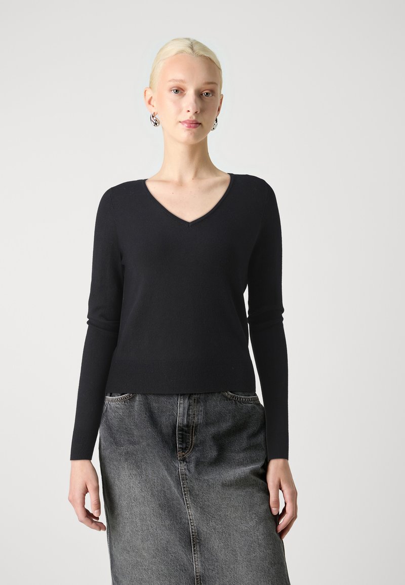 Svart, strikket genser med lange ermer og V-hals design. Materialet virker mykt og glatt. Kombinert med et grått denimskjørt.