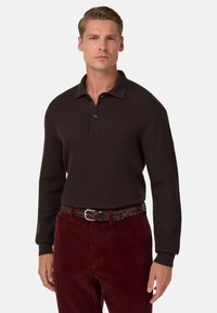 Brunstickad polotröja med ribbad textur och krage, i kombination med vinröda kordbyxor och ett vävt brunt bälte.