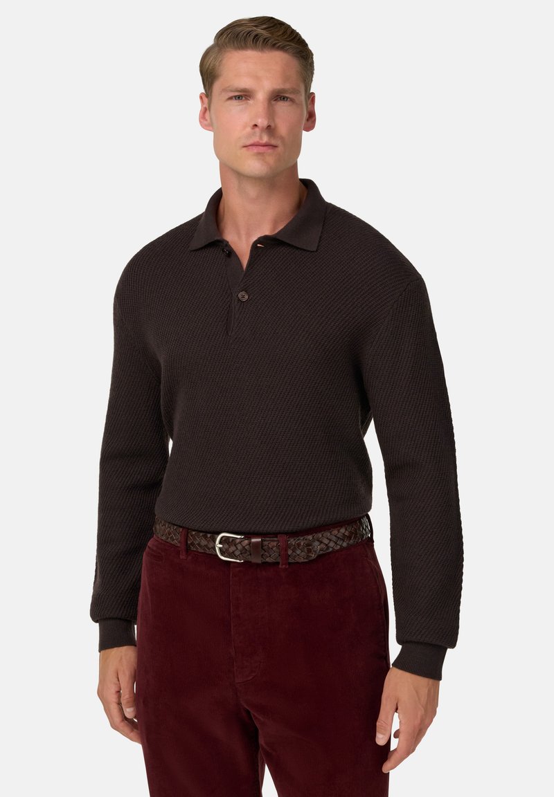 Brunstickad polotröja med ribbad textur och krage, i kombination med vinröda kordbyxor och ett vävt brunt bälte.